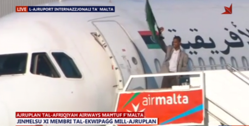 Ir-raġel li  ħareġ mill-ajruplan ixejjer bandiera ħadra, li hi assoċjata mal-Libja fi żmien Gaddafi